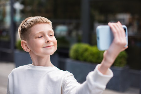 focus on face of smiling boy taking selfie self portrait photos on smartphone, posing on street. boy showing positive face emotionsの写真素材