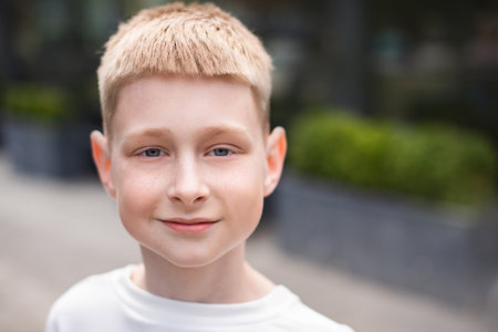 close up portrait of blond boy with blue eyes looking at camera and walking outdoors in cityの写真素材