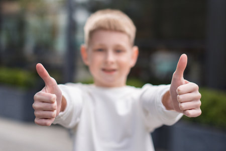 focus on hands of school boy in white sweatshirt show two thumb up gesture on city background. face unfocusedの写真素材