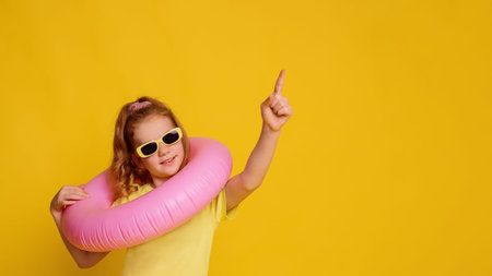 girl in yellow T-shirt mock up point on empty space holing pink inflatable ring on neck over yellow...