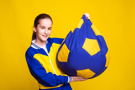 teen girl in sport wear sit in yellow and blue holding bag chair over yellow backgroundの写真素材