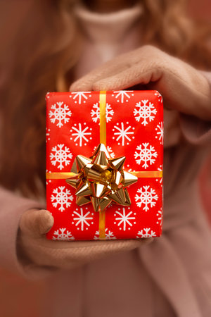 close up christmas present box with golden bow in woman hands in winter gloves. black friday and christmas and new year salesの写真素材