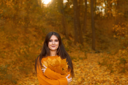 young woman hug self, care about mental health, holding leaves bouquet in autumn parkの写真素材