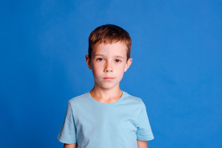 headshot serious schoolboy in blue mockup T-shirt over light blue studio backgroundの写真素材