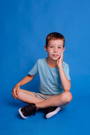 child boy crossed legs, wear blue mockup T-shirt sitting isolated over light blue studio backgroundの写真素材