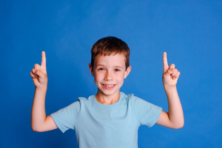 headshot schoolboy point index fingers up to free copy space on light blue studio backgroundの写真素材
