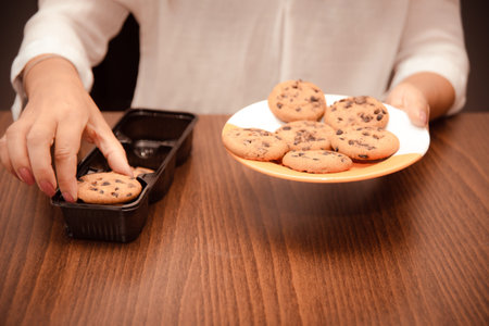 woman transfers crisp chocolate chip cookies from packaging to plate for coffee breakの写真素材