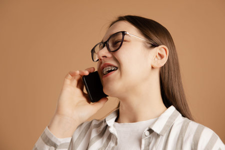woman with braces in glasses talks briskly and resolve issue on smartphone on beige background