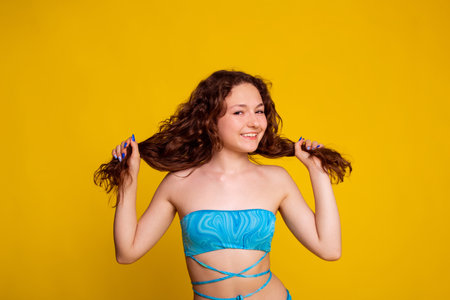 proper curly hair care in summer, teen girl touch wavy hair on yellow background. no split ends hairの写真素材
