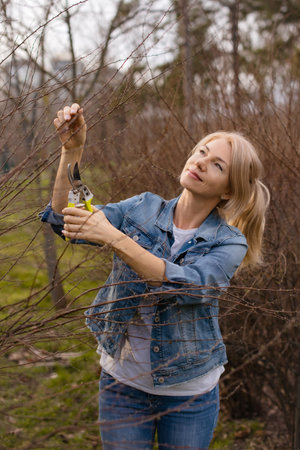 Gardening woman caring for urban shrubs with pruning shears vertical photo