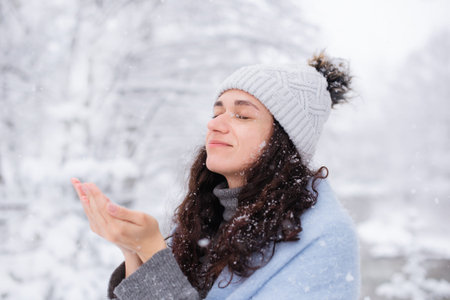 woman catches snowflakes with her palms and enjoys winter weather on walk in forest
