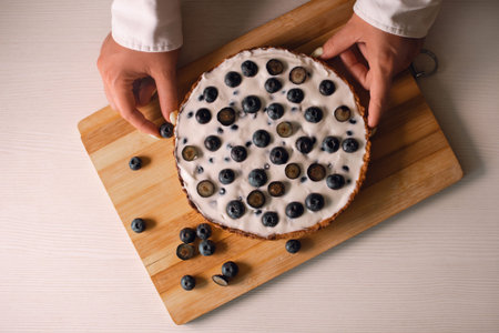 woman chef decorates finished blueberry tart with berries on wooden boardの写真素材