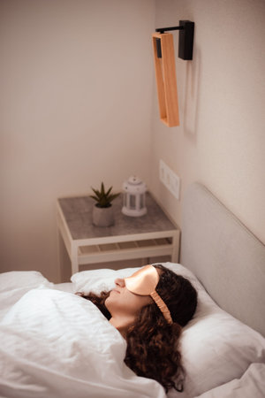 woman wearing beige sleep mask sleeping peacefully in bed in morning