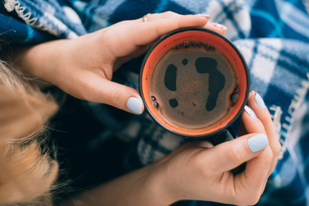 A cup of coffee orange in hands of the girl with a beautiful ornament and beautiful vintage plaid blue plaidの写真素材
