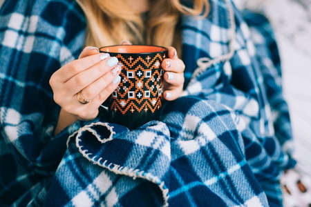 A cup of coffee orange in hands of the girl with a beautiful ornament and beautiful vintage plaid blue plaidの写真素材