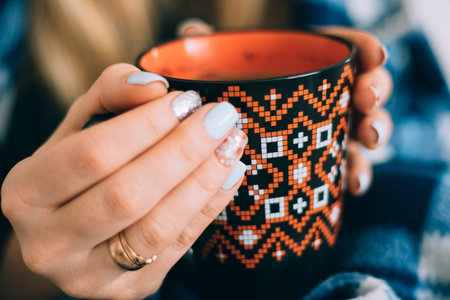 A cup of coffee orange in hands of the girl with a beautiful ornament and beautiful vintage plaid...