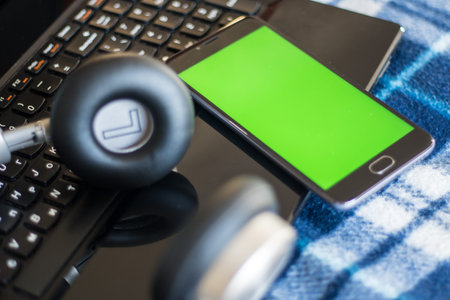 Laptop and headphones smartphone with green screen for key chroma screen. In vintage blue bedspread