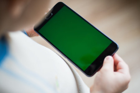 The child is holding a phone in his hand with a green screen for chroma keyer