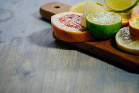 Various citrus fruit cut into slices orange, lemon, lime, grapefruit, pomelo. Spread out on a wooden board on a vintage background of natural wood texturing.の写真素材