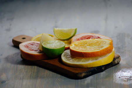 Various citrus fruit cut into slices orange, lemon, lime, grapefruit, pomelo. Spread out on a wooden board on a vintage background of natural wood texturing.の写真素材