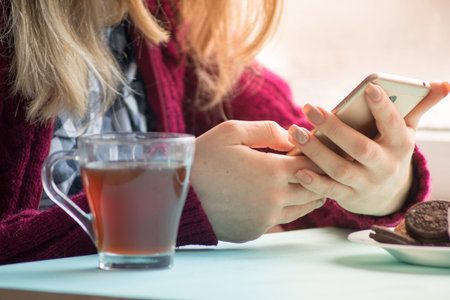 Young woman at cafe drinking and using mobile phone in sunday morning