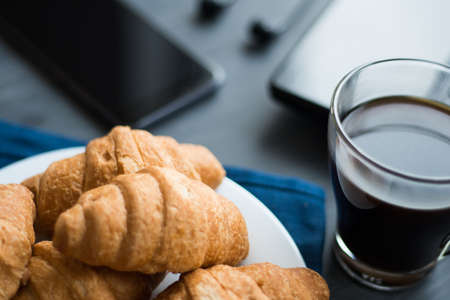 Closeup of wooden desktop with coffee, croissant, phone with headphones and notepadの写真素材
