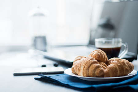 Closeup of wooden desktop with coffee, croissant, phone with headphones and notepadの写真素材
