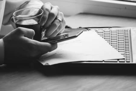 Business man drinking coffee and using laptop computer and mobile smart phone at home, young man browsing internet on phone, e commerce or online working from home, IOT internet of things concept.の写真素材