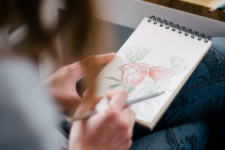 Closeup of women's hand with brush drawing on notepad. Creation process of watercolor paintingの写真素材
