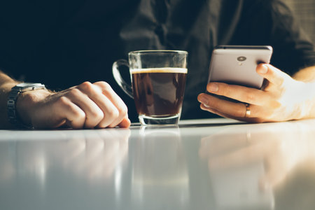 Young man having morning coffee and reading news in his smartphone