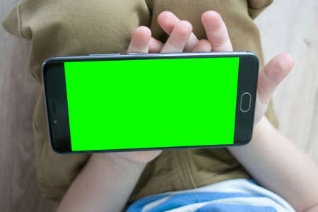 Mock up The child is holding a Smartphone in his hand with a green screen for keying Close-up playing a gameの写真素材