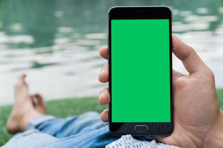 hand of man holding mobile smart phone with chroma key green screen on gren backgroundの写真素材