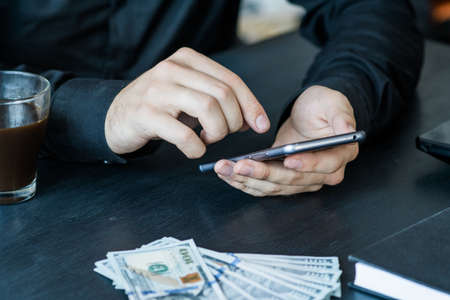 Technology, online banking, money transfer, e-commerce concept. Businessman using smartphone dollar bills flying on grey wall background. Internet earnings conceptの写真素材
