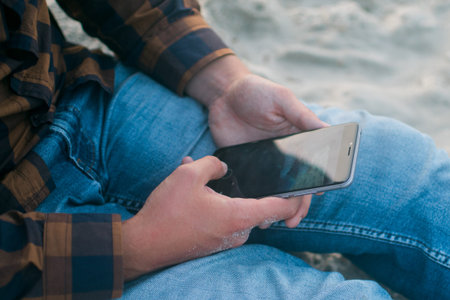 Closeup on person using mobile smartphone over sandy beach background. Photography concept for online connection, communication messaging, banking..の写真素材