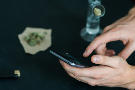 man using a smartphone. Bong and medical marijuana, cannabis thc flower Sativa and Indica Close up...
