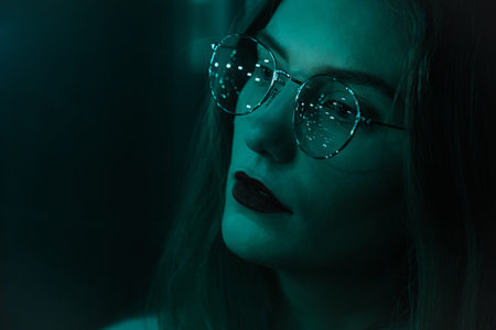 Portrait of a fashionable beautiful girl with glasses in the dark and bokeh. Effect of the focus of...