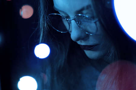 Portrait of a fashionable beautiful girl with glasses in the dark and bokeh. Effect of the focus of the low intensity of sharpness.の写真素材