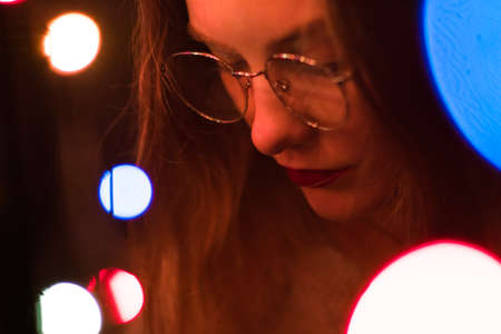 Portrait of a fashionable beautiful girl with glasses in the dark and bokeh. Effect of the focus of the low intensity of sharpness.の写真素材