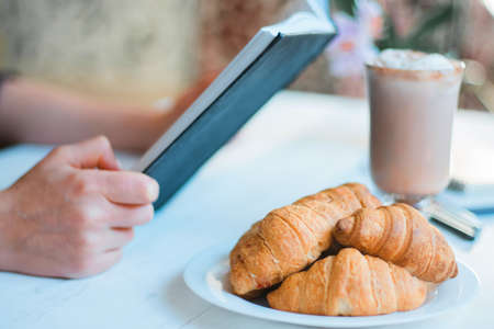 Girl absorbed in reading book during the break in cafe. Cute lovely young woman reading book and drinking coffeeの写真素材