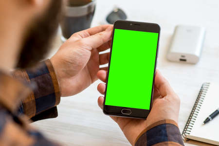 A black smartphone with green screen for chroma key compositing in the hands of a man on a white backgroundの写真素材