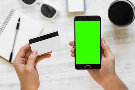 Smartphone with green screen for chroma key compositing and credit card in the hands of a man on a white background, Internet commerce online banking to pay for services and goods inの写真素材
