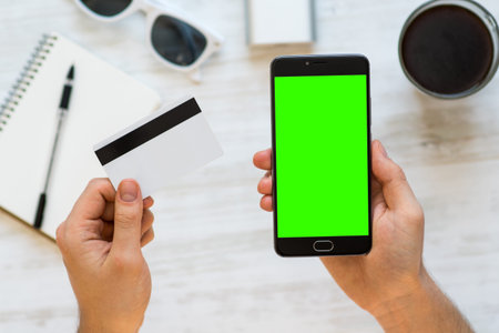 smartphone with green screen for chroma key compositing and a credit card in the hands of a man on...