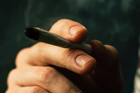 cannabis weed, a joint in his hands A man smokes . Smoke on a black background. Concepts of medical marijuana use and legalization of the cannabis. On a black backgroundの写真素材