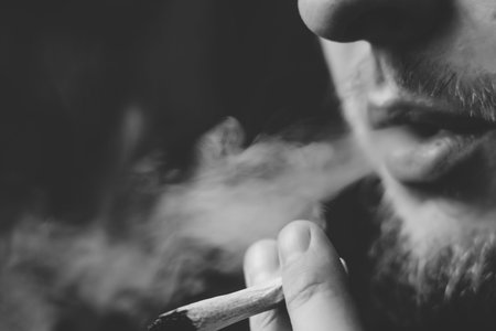 A man smokes cannabis weed, a joint and a lighter in his hands. Smoke on a black background. Concepts of medical marijuana use and legalization of the cannabis. On a black backgroundの写真素材