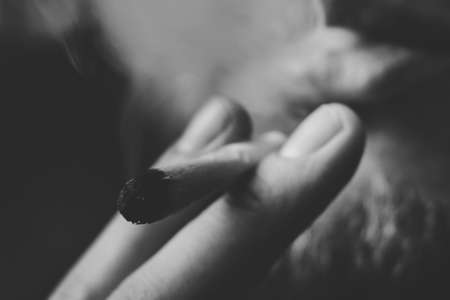 a joint in hand A man smokes cannabis weed, . Smoke on a black background. Concepts of medical marijuana use and legalization of the cannabis. On a black backgroundの写真素材