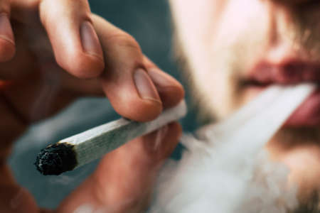 cannabis weed, a joint in his hands A man smokes . Smoke on a black background. Concepts of medical marijuana use and legalization of the cannabis. On a black backgroundの写真素材