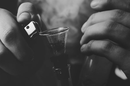 A man smokes cannabis weed, Bong lighter in his hands. Smoke on a black background. Concepts of...