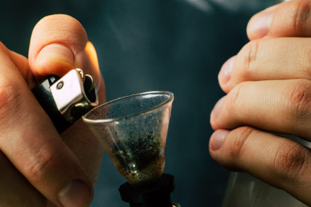 A man smokes cannabis weed, a joint and a lighter in his hands. Smoke on a black background....