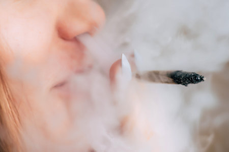 A woman smokes cannabis weed, a joint and a lighter in his hands. Smoke on a black background....