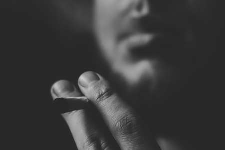 A man smokes cannabis weed, a joint and a lighter in his hands. Smoke on a black background. Concepts of medical marijuana use and legalization of the cannabis. On a black backgroundの写真素材